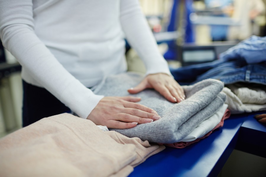 Person folding neatly stacked clothes at a dry-cleaning or laundry counter.