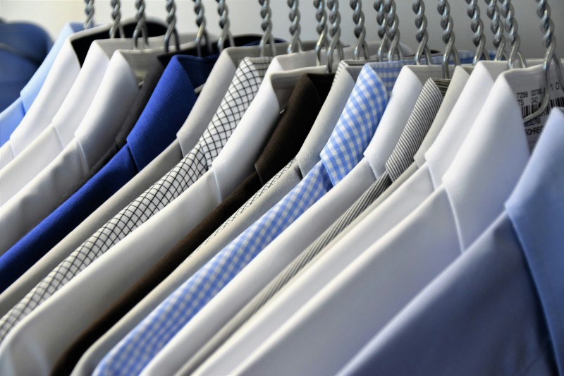 Rows of shirts in various colors and patterns hanging on white plastic hangers in a clothing store