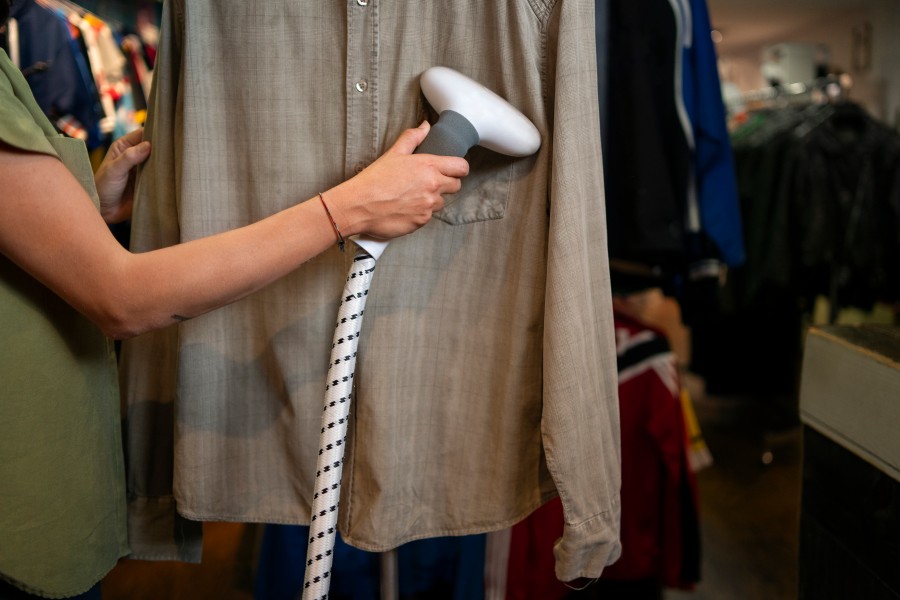 Dry Cleaning Service using a handheld steamer to remove wrinkles from a beige shirt in a clothing store