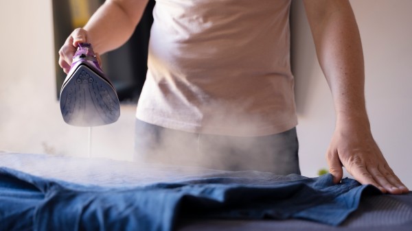 Dry Cleaning Services: Professional ironing of blue clothes with a steam iron for wrinkle-free, fresh-looking garments.